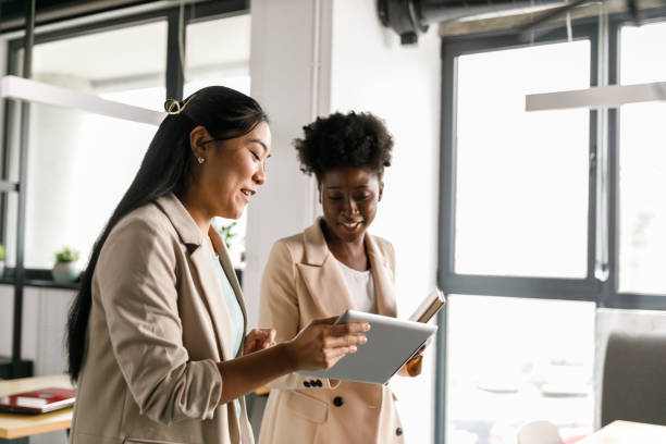 zwei geschäftsfrauen, die während eines meetings daten auf einem digitalen tablet betrachten - people office mobility looking stock-fotos und bilder