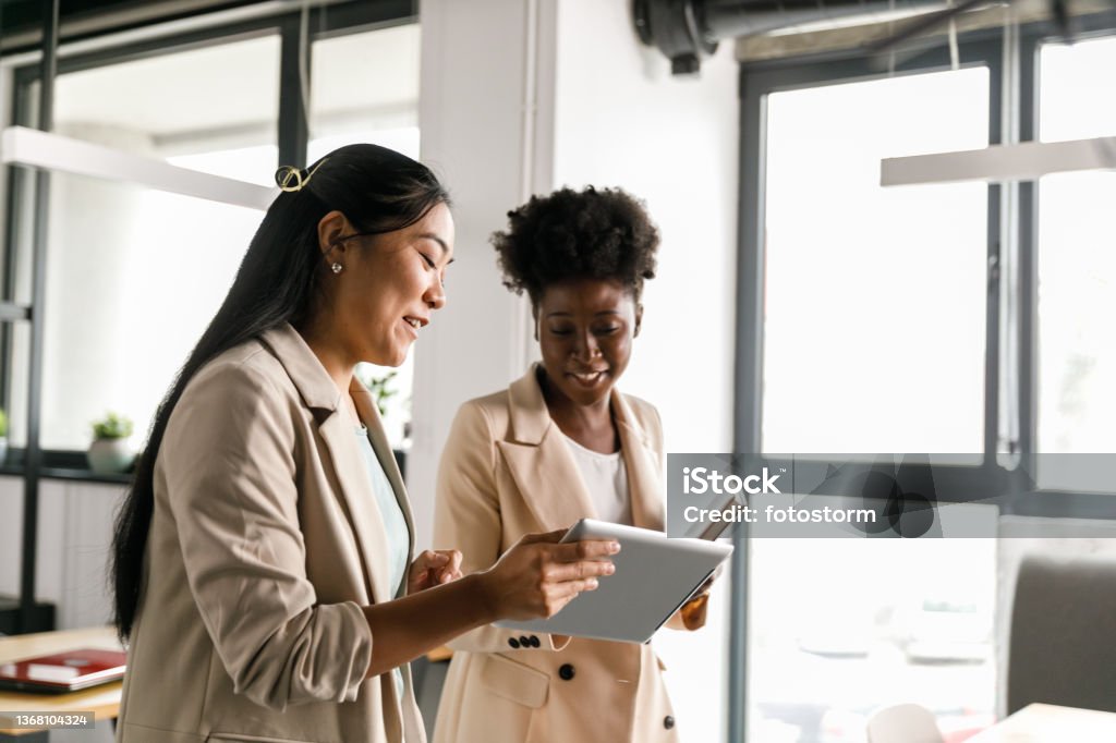 Two businesswomen looking at data on digital tablet while going on a meeting Copy space shot of two young businesswomen walking to a meeting together and looking at data on a digital tablet one of them is holding. Computer Stock Photo