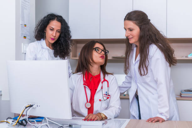 istock ( Medical Team ) Female doctor ( medic ) in her 30's working on her computer while two female nurses stand next to her and discuss a patients illness. 1368105533
