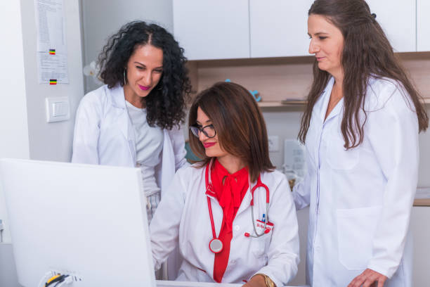 istock ( Medical Team ) Female doctor ( medic ) in her 30's working on her computer while two female nurses stand next to her and discuss a patients illness. 1368105534