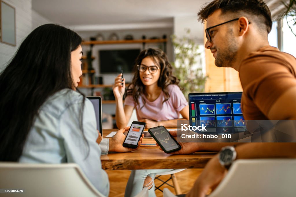 Investing cryptocurrency using smart phone apps Group of friends at home investing in cryptocurrency stock market, using mobile apps for checking progress Cryptocurrency Stock Photo