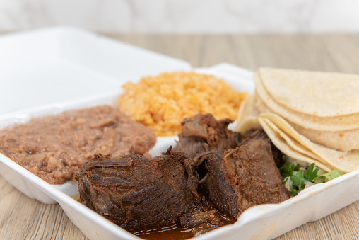Hearty take out order of birria stew meat served to make tacos with the included tortillas, rice and beans in the styrofoam box.