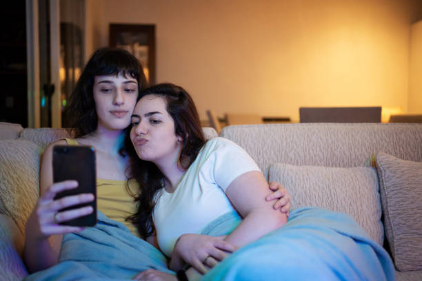 istock Lesbian couple using smart phone and making selfie on the sofa. 1368113147