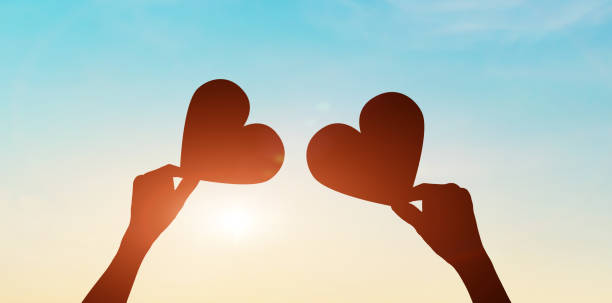 istock Silhouette of hands holding hearts on sunset sky background. 1368118778