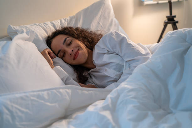 Latino beautiful woman lying down on bed in bedroom in dark night room. Attractive young female in pajamas sleeping alone on comfortable pillow and cozy blanket in quiet room for health care at home. stock photo