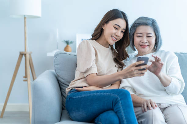 famiglia adorabile asiatica, figlia giovane usa il telefono cellulare con la madre anziana. bella ragazza e donna anziana anziana siedono sul divano, godono di shopping online sul sito internet insieme nel soggiorno a casa. - senior adult child holding grandparent foto e immagini stock