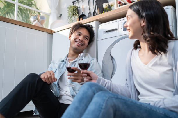 um jovem casal asiático passa um tempo juntos na cozinha de casa. homem e mulher românticos atraentes se sentam no chão para beber vinho para celebrar a vida familiar e se mudar para uma nova casa. - japanese ethnicity heterosexual couple men smiling - fotografias e filmes do acervo