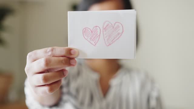 Woman showing a white paper with coloring red heart shape by crayon