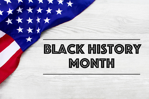 Black History Month  written on a  white  wood background, with an American flag.