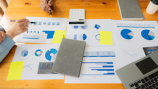 Team meeting to plan a modern and conceptual office design. Hands of businesspeople working on financial graph documents and calculator laptop to discuss the market situation, top view.