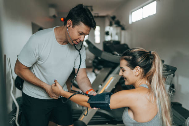 Personal trainer checking athlete's blood pressure at gym stock photo