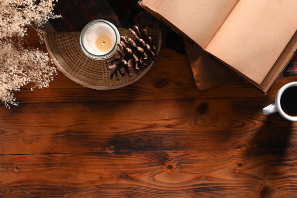 Top view vintage book, coffee cup, candle and pine cone on wooden table.