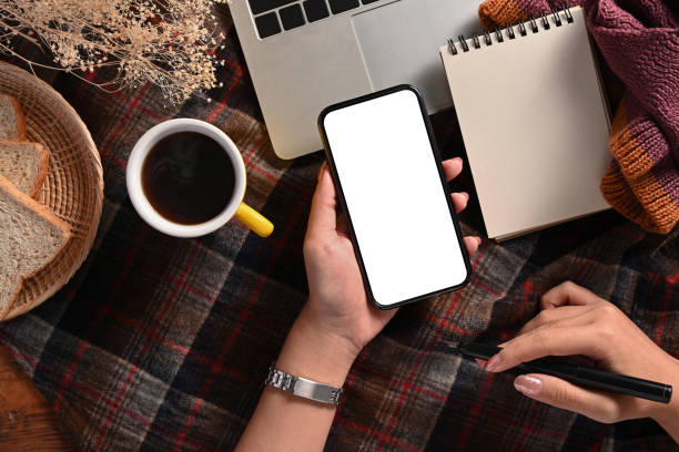 istock Above view woman holding pen and using smart phone on plaid background. 1368138058