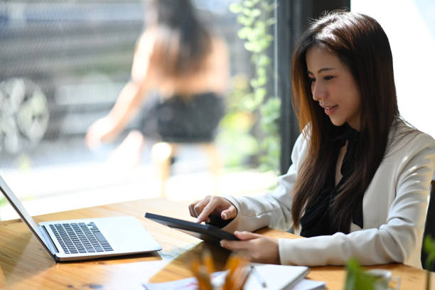 istock Smiling asian woman entrepreneur using digital tablet while sitting at modern workplace. 1368138091