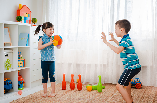 native children boy and a girl play in a children's game room, throwing ball. concept of interaction siblings , communication, mutual play, quarantine, self-isolation home, brother sister.