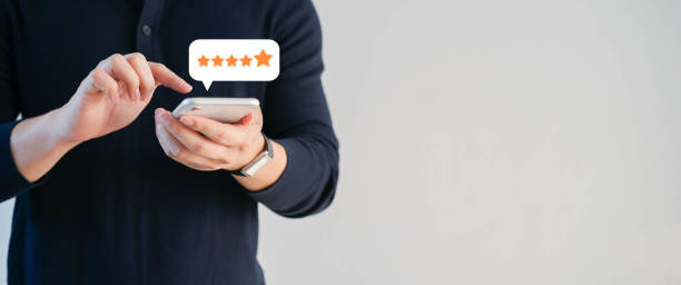 close up on customer man hand pressing on smartphone screen with  five star rating feedback icon and press level excellent rank for giving best score point to review the service , technology business concept stock photo