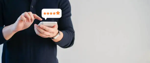 close up on customer man hand pressing on smartphone screen with  five star rating feedback icon and press level excellent rank for giving best score point to review the service , technology business concept