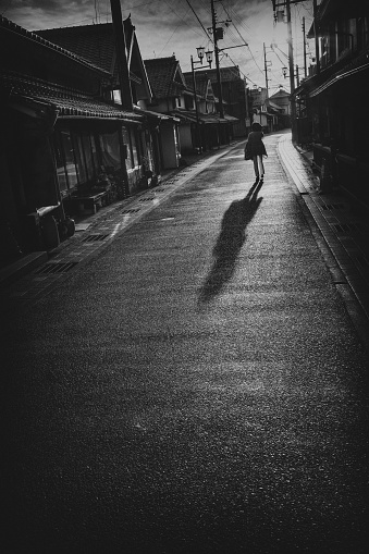 Silhouette of a woman walking in a Japanese alley towards the setting sun