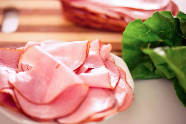 istock Ham slices on a white plate, salad leaves and a cutting board with stack of ham in the background 1368146366