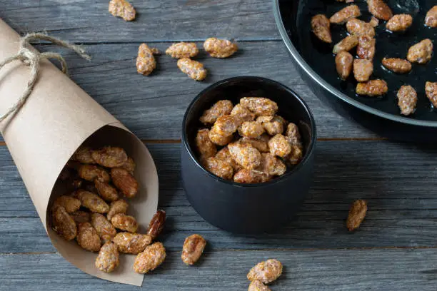 sweet food, candy, caramelized nuts with butter, sugar and cinnamon in treat paper bags and in a pan