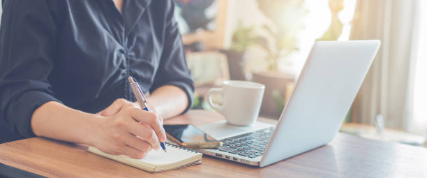 istock Woman hand writing on a notepad with a pen and use a laptop computer in the office. 1368154377