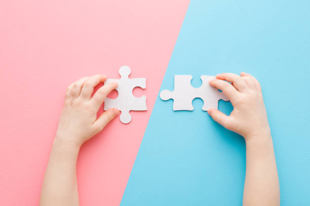 istock Baby hands playing and putting together white puzzle pieces on light blue pink table background. Pastel color. Closeup. Point of view shot. Children development. Two sides. Top down view. 1368154513