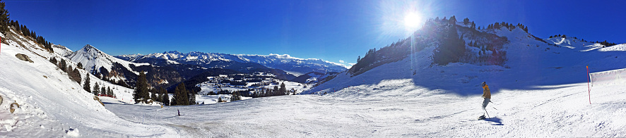Skiers enjoy the panoramic slopes of Morzine, French Alps, France. The fresh piste snow of Morzine ski resort in the winter sunshine under a blue clear sky