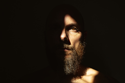 Dramatic light self portrait: bearded man in the shadow. Half of the face is illuminated by sunlight, the other is in the dark