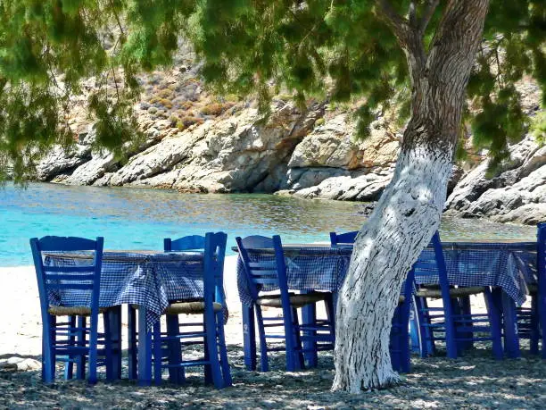 Typical Greek summer landscape!! Tavern by the sea, with traditional blue wooden tables and chairs under the shadow of  tamarisk (almyrikia) trees, Sefiros Island, Cyclades, Greece.
