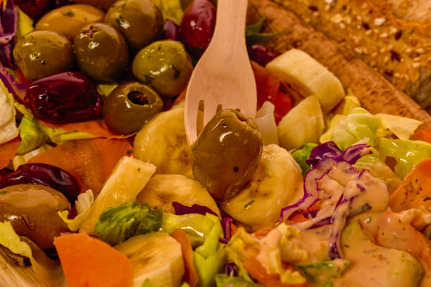 a bowl with assorted salad, olives, bananas and sauce.