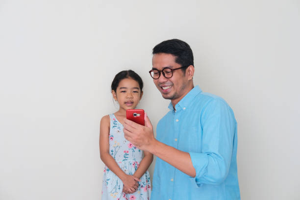 Asian father smiling happy while showing  mobile phone screen to his daughter Asian father smiling happy while showing  mobile phone screen to his daughter keluarga stock pictures, royalty-free photos & images