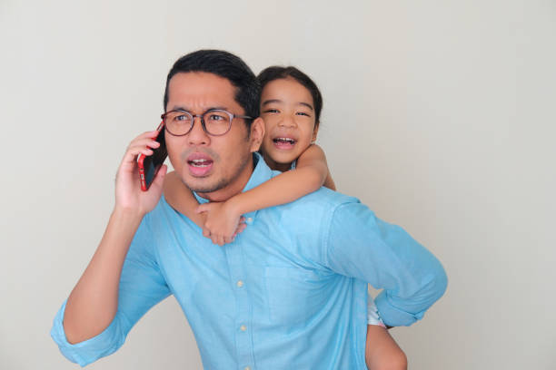 Asian father carry his daughter in the back while answering a phone call Asian father carry his daughter in the back while answering a phone call keluarga stock pictures, royalty-free photos & images