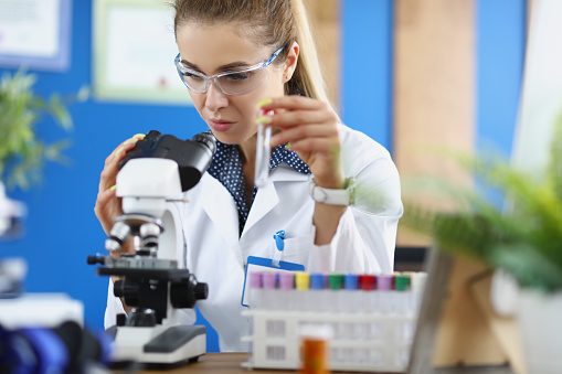 Woman scientist chemist looking through microscope and holding test tube. Laboratory diagnostics of internal diseases concept