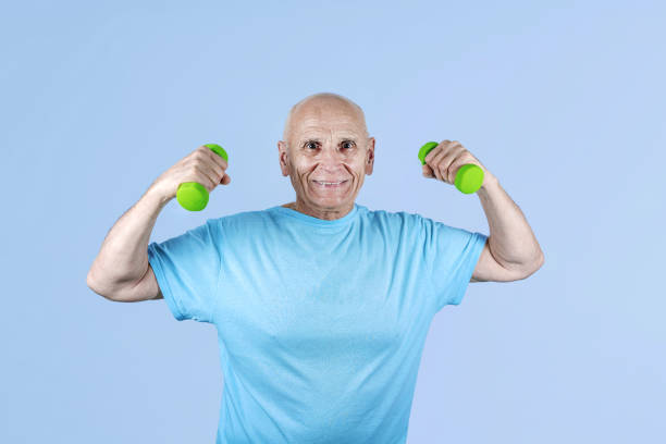 Smiling excited cool pensioner practising bodybuilding exercising holding green colored dumbbells. Body care and lifestyle concept.