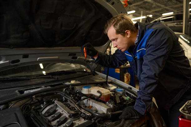 istock Concentrated Caucasian young man, car engineer technician mechanic in professional uniform, automobile mechanic repairman testing and checking oil level in the car engine. Car service and maintenance 1368173293