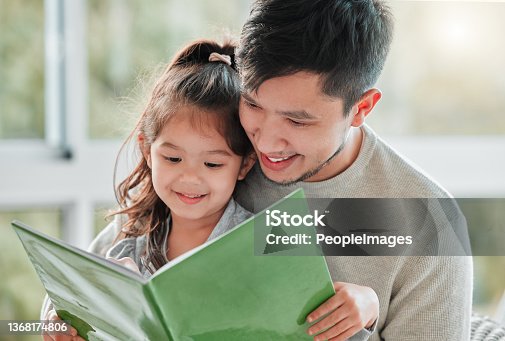 istock Shot of of a little girl sitting on her father's lap with a book 1368174806