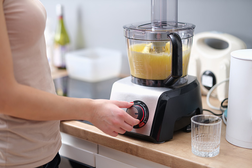 Woman cook turning on button of food processor for kneading dough closeup. Household appliances as assistant in cooking concept