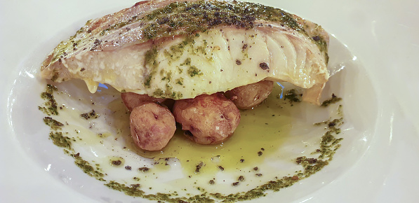 Portion of roasted fish steak, red snapper, and whole cooked potatoes with parsley.