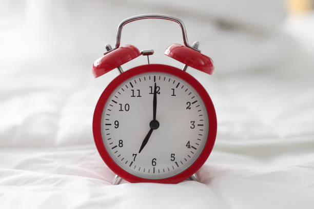istock Red alarm clock for 7 hour standing on white bed closeup 1368176204