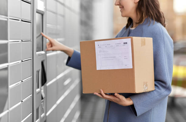 smiling woman with box at automated parcel machine stock photo