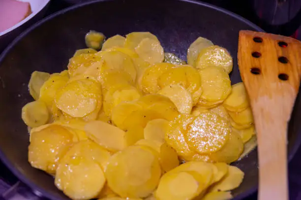 fried potatoes with a wooden spoon in a pan close-up