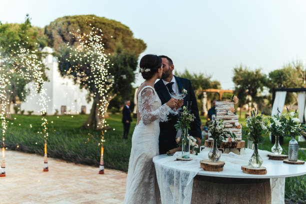 corte de pastel durante la ceremonia de la boda con fuegos artificiales de fondo - boda fotografías e imágenes de stock