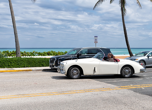 Palm Beach, Florida USA - March 21, 2021: man driving white Classic Jaguar XK 150 3.8 Roadster retro car in palm beach, united states of america. left side view.
