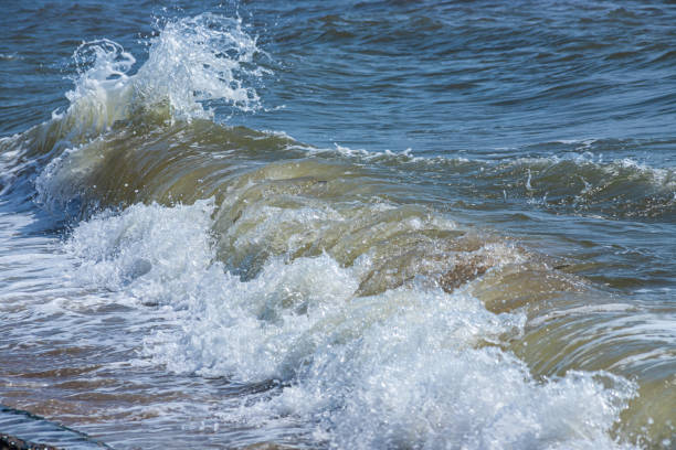 Sea waves crash against large rocks on the shore, forming large splashes..