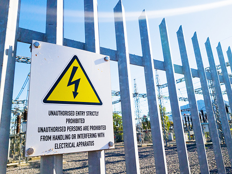 High-voltage power equipment behind a fence and warning sign.