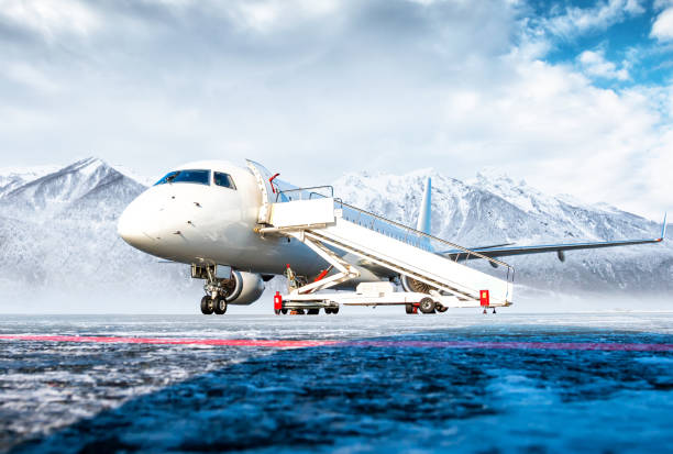 weißes passagierflugzeug mit lufttreppe am flughafenvorfeld vor dem hintergrund hoher malerischer berge - airfield mountain snow airport stock-fotos und bilder