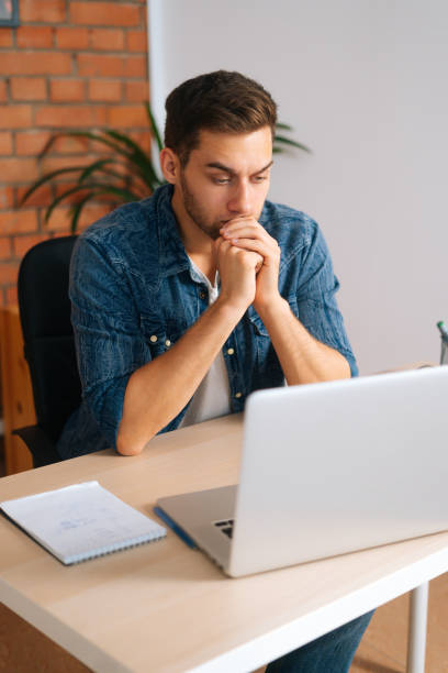 istock Vertical high-angle view of frustrated handsome freelance programmer male in wireless earphone working on laptop computer sitting at desk 1368183021