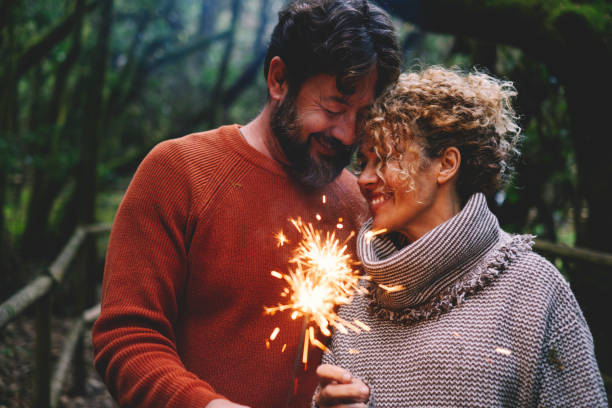 Romantic adult couple enjoy and love together with fire sparkler light in the forest green trees background. Man and woman with tenderness and relationship celebrate with firelight and smile stock photo