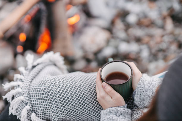 istock Camper holding cup of tea next to campfire 1368186680