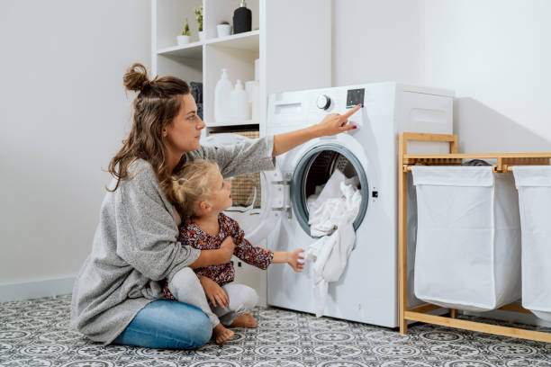 istock Woman spends time with young child in laundry room, bathroom, performs household duties while on maternity leave, takes care of daughter, shows girl how to operate washing machine 1368187314